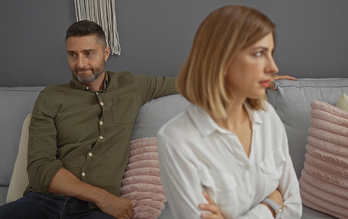 A couple sitting at opposite ends of a sofa, each looking away from the other