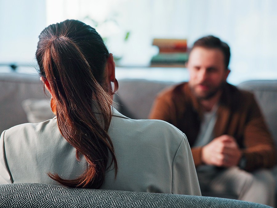 A therapist seen from behind, listening to a client sitting across from her