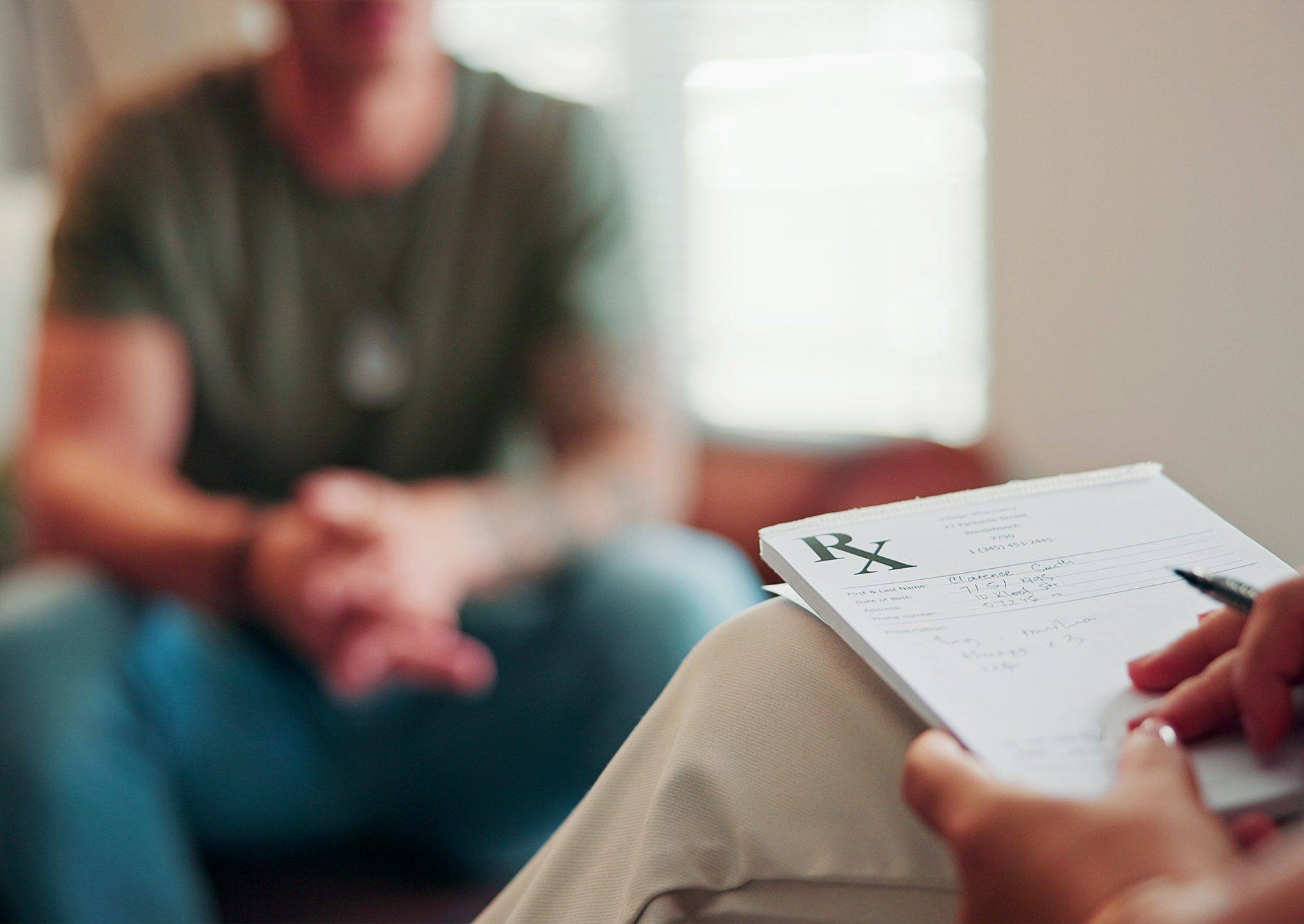 A therapist writing on a prescription pad while a client talks