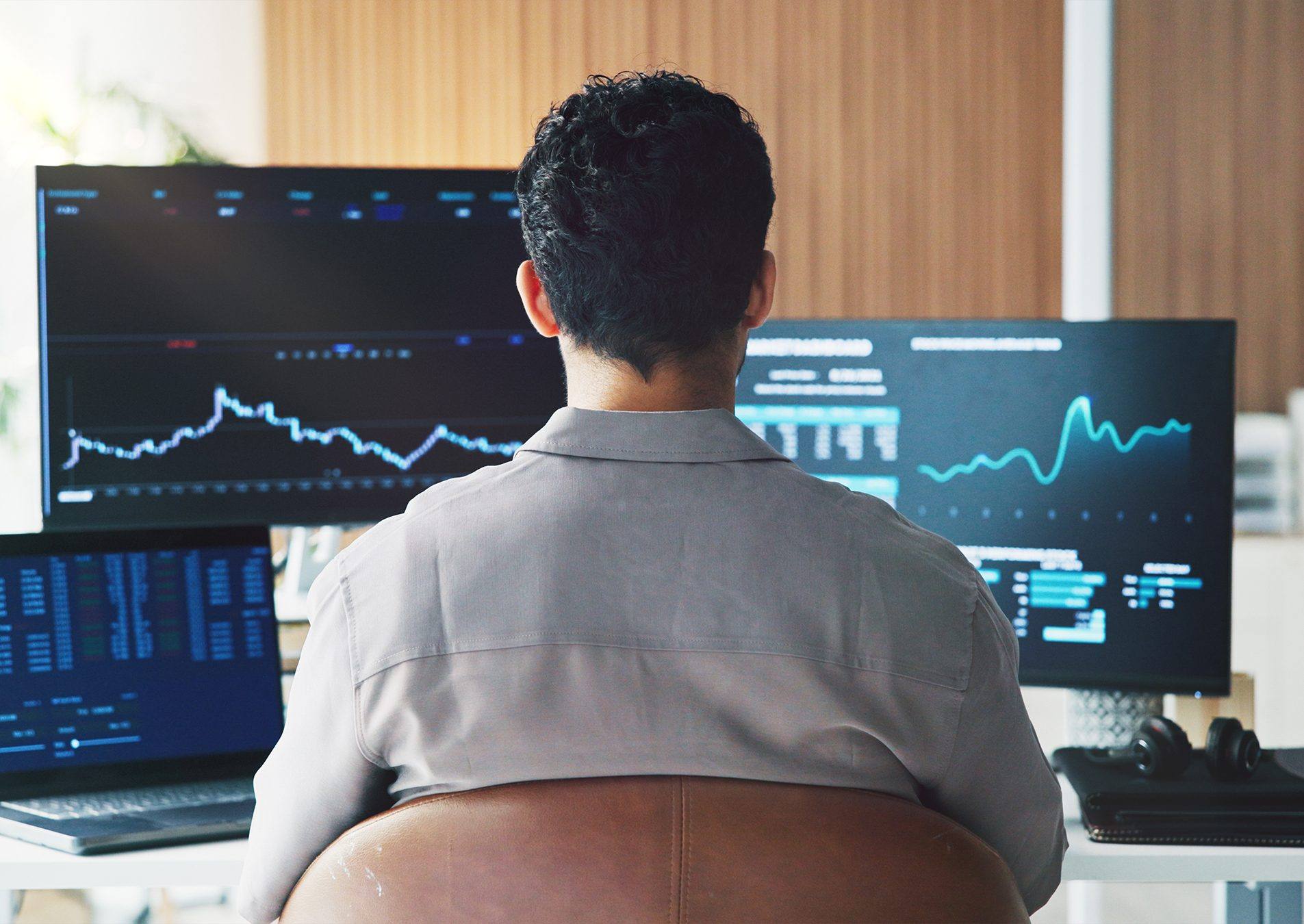 A financial professional at a desk of monitors showing market charts
