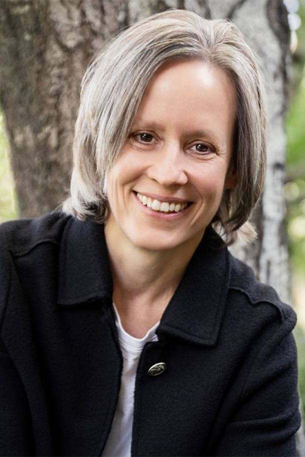 Sarah Swantner smiling, standing outdoors against a tree in dappled natural light
