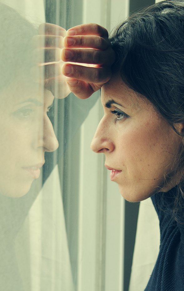 A woman in profile at a window, a hand pressed to the glass behind her