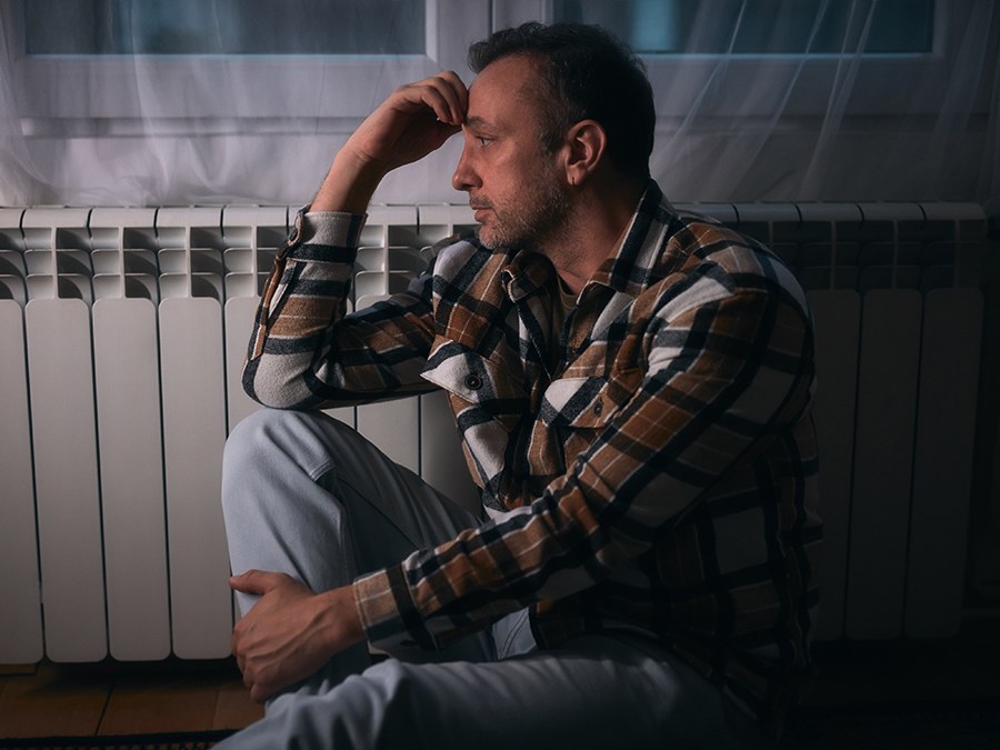 A man sitting on the floor beside a radiator at night, head resting on his hand