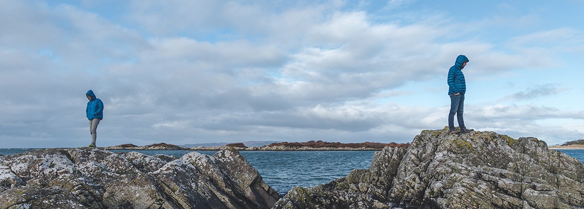 Two people standing on separate rocky outcrops with open water between them