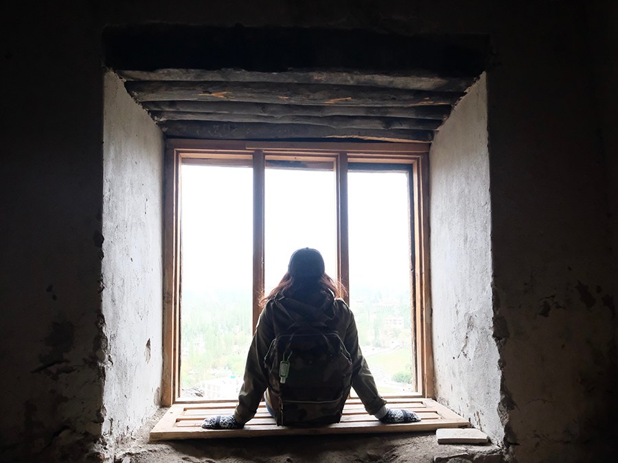 A person sitting alone in a bright stone window opening, framed by a dark room