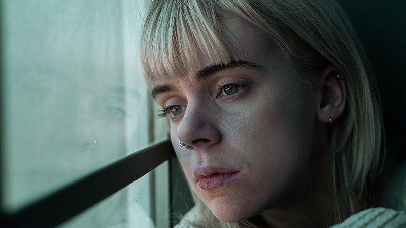 A woman resting her head against a train window, looking out