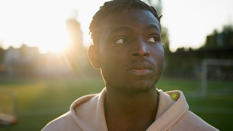 A young man outdoors in low evening sun, looking up and away from the camera