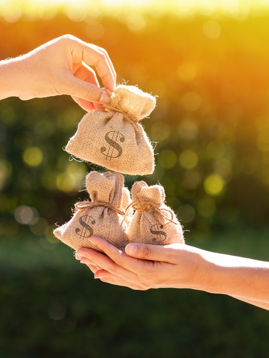 One pair of hands passing small money bags into another pair of cupped hands in evening light