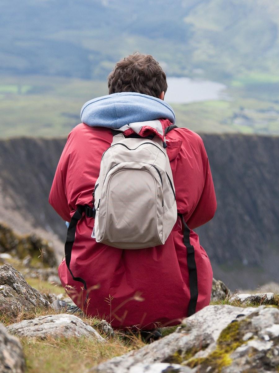 A person sitting alone on a rocky summit, looking out over a green valley and lake
